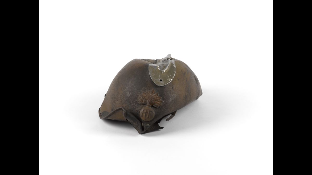 Casque Adrian modèle 1926 d’infanterie du sous-lieutenant Raymond de Pourtalès - Sous-lieutenant au 4e régiment d’infanterie, il est arrêté le 28 mai par les Allemands au carrefour du Touquet. Refusant de se rendre, il sort son revolver mais tombe sous les balles. Après l’avoir enterré avec les honneurs militaires, les Allemands posent sur sa croix ce casque Adrian déformé, témoin de la violence des combats de mai-juin 1940. / Paris, musée de l’Armée, inv. 14200. Don de Mlle de Pourtalès © Paris - Musée de l'Armée, Dist. RMN-Grand Palais / Marie Bruggeman